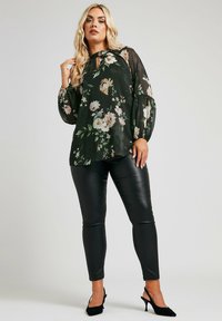 Blusa a stampa floreale verde scuro con scollatura a chiave e maniche a palloncino, abbinata a pantaloni attillati in pelle nera e tacchi a slingback neri.