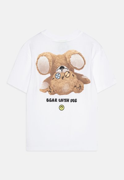Hvit T-skjorte med korte ermer som fremhever et mykt teddy-bjørn grafikk med knappe-øyne, svart tekst med «BEAR WITH ME», og et smilende ansikt.