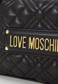 Svart quiltad läderhandväska med en guldfärgad "LOVE MOSCHINO" logotypplatta och dekorativa metallaccenter.