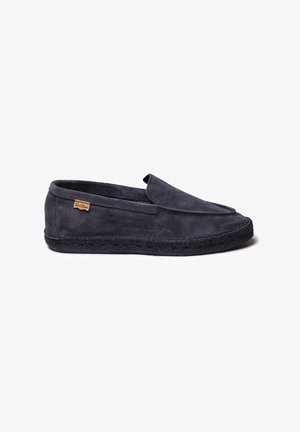 Zapato slip-on de ante en gris oscuro con suela de cuerda negra trenzada. Presenta un diseño cosido y una pequeña etiqueta de marca en el lateral.