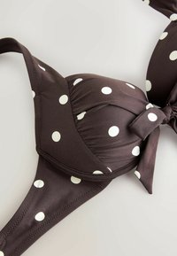 Top bikini a pois marroni con forma triangolare, supporto con ferretto e dettaglio del nodo frontale. Spalline regolabili per un miglior adattamento e comfort.
