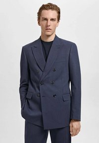 Blazer croisé bleu marine avec des boutons noirs, à revers crantés, et une poche poitrine, en tissu lisse avec une coupe ajustée.