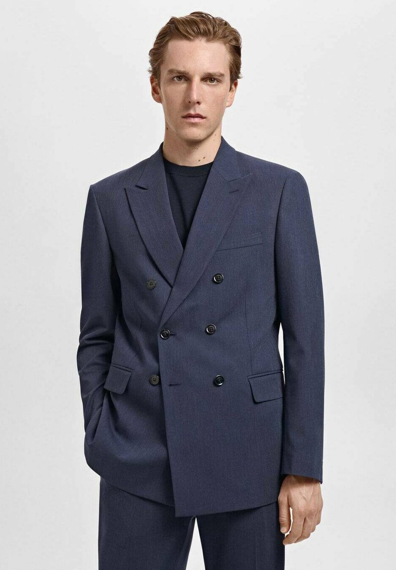 Blazer croisé bleu marine avec des boutons noirs, à revers crantés, et une poche poitrine, en tissu lisse avec une coupe ajustée.