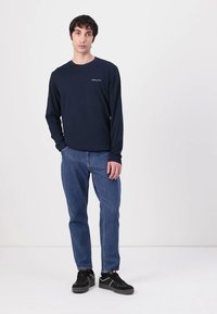 Marineblå langermet skjorte med en liten logo, kombinert med lyseblå jeans og svarte joggesko. Enkelt design og behagelig passform.