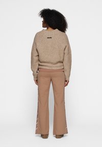 Suéter beige de punto con mangas anchas, combinado con pantalones marrón claro con rayas de satén a los lados. Diseño texturizado y de ajuste relajado.