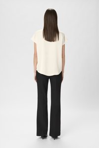 Cream short-sleeve blouse with a curved hem, paired with black, flared trousers. The top has a smooth texture and a relaxed fit.