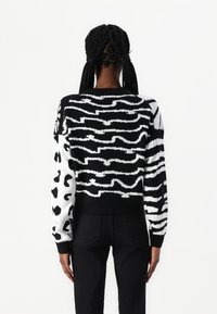 Black and white knitted sweater featuring a mixed pattern of zigzags and animal prints, with ribbed cuffs and hem. Back view shown.