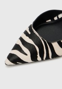 Pointed-toe flat shoe in black and beige zebra print with a textured, fur-like exterior and smooth black interior.