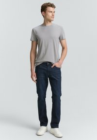 Camiseta gris de cuello redondo combinada con pantalones vaqueros de color azul oscuro; los vaqueros tienen un corte recto. El calzado consiste en zapatillas blancas.