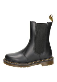 Botín Chelsea negro de cuero con panel elástico en los laterales, costura amarilla en la suela y tira en el talón con la marca.