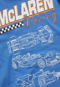 Niebieski t-shirt z białą ilustracją samochodów wyścigowych, z napisem "McLaren Racing" w wyrazistym pomarańczowym kolorze oraz czarno-białym wzorem w kratkę.