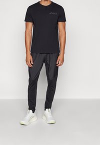 T-shirt de sport noir avec un logo discret, associé à un pantalon jogger noir au toucher lisse et des baskets blanches avec des accents néon.