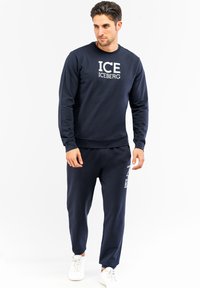 Felpa navy e pantaloni jogger abbinati con logo "ICE ICEBERG", collo a giro, polsini a costine e grafiche laterali sui pantaloni. Sneakers bianche.
