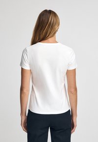 Hvid bomulds T-shirt med korte ærmer og rund halsudskæring, med en glat overflade og en tætsiddende silhuet, vist fra ryggen.