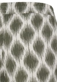 Tissu blanc avec motif abstrait de losanges vert olive et de coups de pinceau verticaux, mettant en valeur une ceinture élastique froncée.