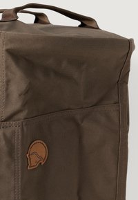Saco de armazenamento em tecido castanho com um acabamento texturizado, apresentando um logótipo de pele cosido e duas alças superiores para facilitar o transporte.