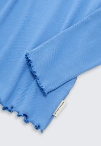 Vaaleansininen ribbineuloskangas, jossa on salaatinreunaiset helma ja hihansuut, ja siinä on pieni valkoinen etiketti, jossa lukee "Tom Tailor".