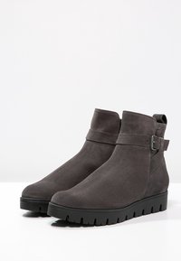 Bottines en daim gris avec un bout arrondi, fermeture éclair sur le côté et détail de sangle à boucle. Semelle noire épaisse avec un motif de traction texturé.