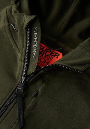 Sudadera con capucha verde oliva con cremallera completa, con la marca "SUPERDRY" en el tirador de la cremallera y en el cuello, que presenta una etiqueta roja en el interior del escote.