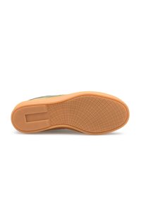 Podeszwa buta w jasnobrązowej gumie, z fakturowaną powierzchnią o wzorze kratki i płaskim kształcie. Górna część niewidoczna.