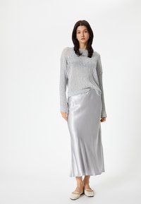 Maglione a coste grigio chiaro con maniche lunghe, abbinato a una gonna midi in satin argento lucido e ballerine color crema. Tessuto morbido, vestibilità rilassata.