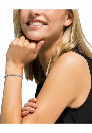Sølvarmbånd med runde rhinsten, båret på et håndled. Hånden er placeret nær hagen, hvilket viser armbåndets detaljer.