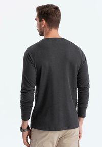 Dunkelgraues langärmliges Shirt aus geripptem Material mit Rundhalsausschnitt und Raglansleeves. Vor einem neutralen Hintergrund platziert.