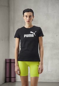 Melnas īsām piedurknēm t-krekls ar baltu "PUMA" logo, saskaņots ar spilgti dzeltenām pieguļošām šortiem. Gluda auduma, vienkāršs dizains, sportiska piegriezuma.
