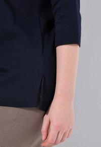 Top in cotone blu navy con maniche a tre quarti, dettagli con spacchi laterali e vestibilità ampia, abbinato a tessuto beige chiaro.