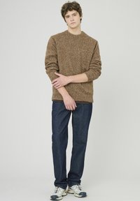 Pull en tricot texturé brun avec un col rond, associé à un pantalon en denim foncé et des baskets claires. Design simple et décontracté.