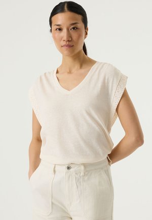 Top beige claro con escote en v y mangas cortas con ribetes de encaje, hecho de tela suave, combinado con pantalones crema de talle alto.