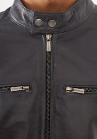 Svart läderjacka med ståkrage, frontdragkedja och två fickor med dragkedja i silverfärgade detaljer. Slät textur.