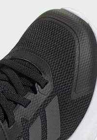 Black athletic shoe with a textured mesh upper, reinforced rubber accents, and flat black laces. Features a white outsole and logo detailing.