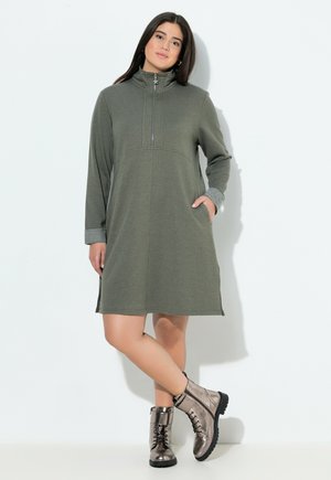 Khaki vihreä vetoketjullinen mekko pitkilla hihoilla, sivutaskuilla ja harmailla hihansuilla. Yhdistetty kiiltäviin metallisiin nilkkasaappaisiin, joissa on nauhat.