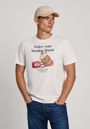 T-shirt in cotone bianco con grafica di un bulldog e la scritta "Goditi il tuo arrosto della domenica", abbinato a un cappello beige.