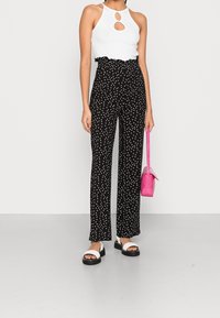 Haut sans manches blanc avec une découpe en trou de serrure, assorti à un pantalon noir taille haute avec des pois blancs. Un petit sac à main rose complète le look.