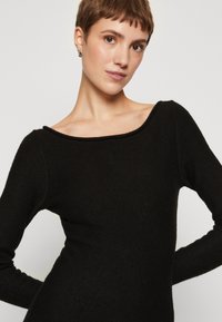 Black long-sleeve knit top with a wide scoop neckline, fitted body, and subtle texture. Features a smooth, soft fabric.