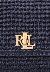 Ναυτικό πλεκτό τσάντα με υφή, που διαθέτει χρυσό λογότυπο RL στην μπροστινή πλευρά, τονίζοντας μια δομημένη, ορθογώνια μορφή.