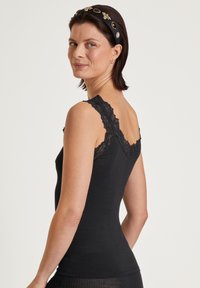 Top aderente nero a costine con bordo in pizzo lungo le spalline, dalla forma sagomata e dalla consistenza morbida. Mettesse in risalto il décolleté e le spalle.