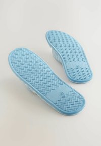 Et par lyse blå slippers med teksturerede gummisulder, der har et zigzag-mønster, blødt stofoverdel og åbent bagdesign.