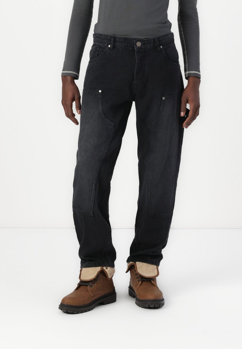Svarte denim cargo-bukser med løs passform, med flere lommer og metallic detaljer. Kombinert med brune snøresko.