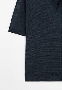 Polo tričko s krátkým rukávem v tmavě námořnické modři. Tkaná struktura, design s výstřihem do V, žebrované manžety a lem. Minimalistický a moderní styl.
