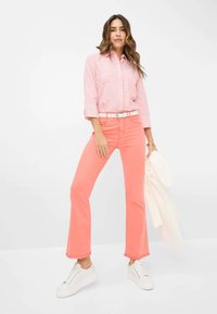 Roze en witte gestreepte button-up shirt, gecombineerd met helderroze flared jeans en witte sneakers. Opvallende rafelranddetail op de jeans.