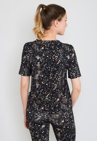 Korte mouwen, zwart top met een luipaardprint patroon in tan en wit. Zacht, elastisch materiaal met een relaxte pasvorm.