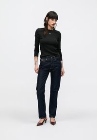 Svart genser med lange ermer og rund hals, kombinert med mørkeblå jeans med rette ben. Modellen har på seg burgunderrøde høyhælte sko.