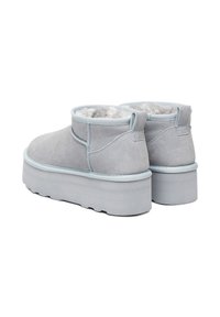 Botine din suede gri deschis cu platformă, căptușite cu un material moale în interior și cu fante la călcâie, văzute din spate și ușor în unghi.