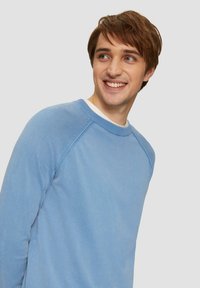 Hellblaues Sweatshirt aus Baumwolle mit Rundhalsausschnitt und Raglanärmeln. Verfügt über gerippte Manschetten und Säume, eine glatte Textur und minimale Nähte.