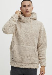 Light beige fleece pullover hoodie with a zippered neck, adjustable drawstrings, and a front kangaroo pocket. Textured, soft fabric.
