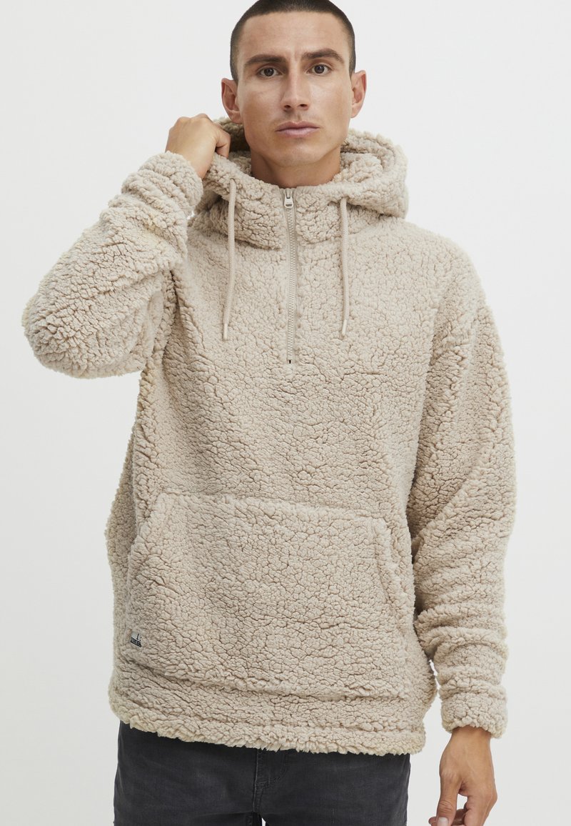 Light beige fleece pullover hoodie with a zippered neck, adjustable drawstrings, and a front kangaroo pocket. Textured, soft fabric.