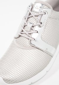 Baskets gris clair avec une tige en mesh, des accents argentés brillants et des lacets ronds. Elles possèdent une semelle en caoutchouc et un motif texturé.